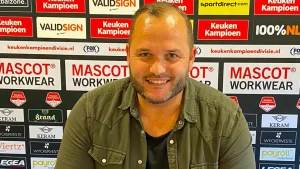 Nieuwe trainer Rico Goffin van FC Gulpen poseert lachend voor een sponsorwall in het Roda JC stadion